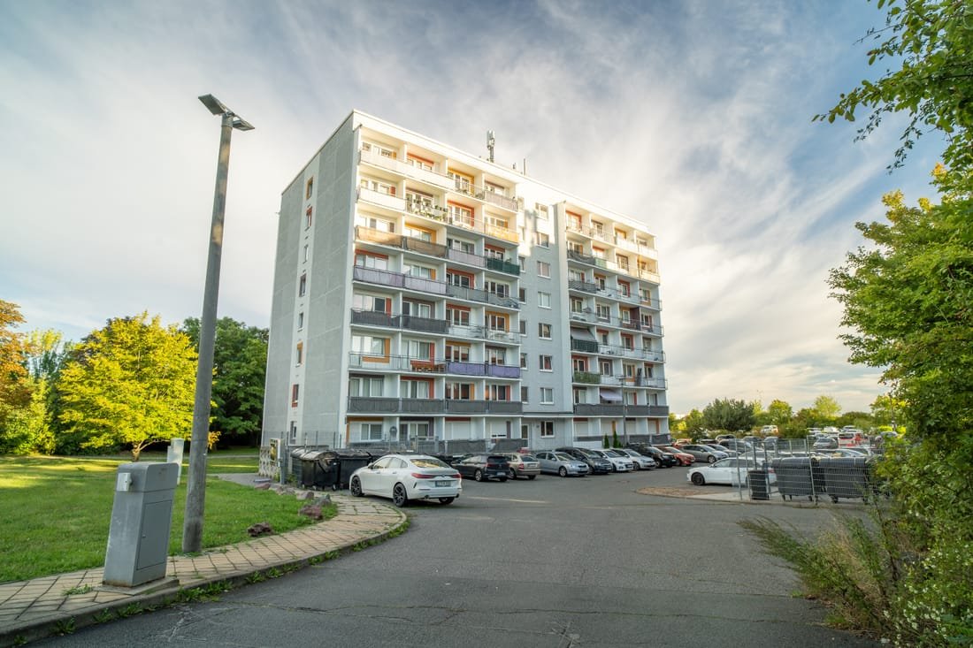 Wohnhochhaus mit Balkonen, davor Stellplätze und eine Rasenfläche